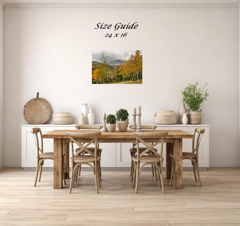 Mockup of a 24 by 16 inch autumn mountain landscape print displayed on a dining room wall above a wooden table.