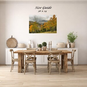 Mockup of a 36 by 24 inch autumn mountain landscape print displayed on a dining room wall above a wooden table.