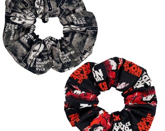 Puede incluir: Dos scrunchies negros con temática de película de terror. Un scrunchie tiene un estampado en blanco y negro con el texto "The Nightmare Isn't Over" y el otro scrunchie tiene un estampado en negro y rojo con el texto "There Is No Place To Hide".