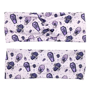 May include: Two purple and white patterned headbands with a coffin and cross design. The text on the headband reads "Wish You Were Here" and "Pretty Dead".