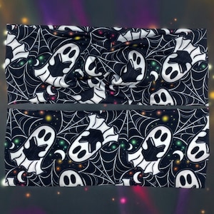 May include: Two Halloween-themed headbands. The headbands feature a black background with white spiderwebs and cartoon ghosts. The ghosts have a friendly expression. The design also includes small colorful stars and moons.