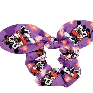 May include: Purple scrunchie with a repeating pattern of Mickey Mouse and Minnie Mouse holding hearts that say "True Love" and "So Much Love".