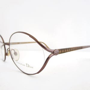 May include: A pair of brown metal eyeglasses with a rounded, oval-shaped frame. The glasses have a Christian Dior logo on the side.