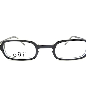 May include: Black rectangular eyeglasses with the brand name "ogi" printed on the left lens. The frames are a matte black, and the lenses are clear. The glasses have a classic, minimalist design.