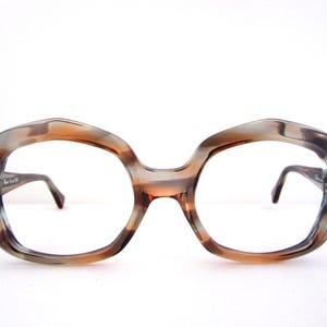 May include: Vintage oversized eyeglasses with a marbled brown and gray pattern. The frames have a unique, rounded shape with dark temples and nose pads. A stylish accessory.
