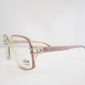 May include: Clear plastic eyeglasses with a pink and gold frame. The frame has a textured design and the brand name "C.D. WETZLER INTERNATIONAL Classic" is printed on the side.