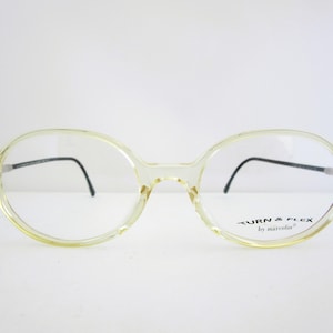 May include: Clear, round, yellow-tinted eyeglasses with black arms and a "TURN & FLEX by marcolin" label on the right arm.