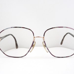 May include: A pair of spectacles with a burgundy and gold frame. The frame has a geometric shape and the lenses are clear.