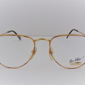 Può includere: Occhiali da vista in metallo dorato con montature a motivo tartaruga. Il nome del marchio "En Vue!" è stampato sulla lente destra.