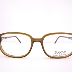 Puede incluir: Gafas de pasta de carey marrón con lentes transparentes. La montura tiene el logotipo de Bulova y el texto "Tribute Collection".