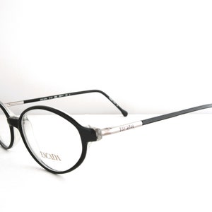 May include: Black oval-shaped eyeglasses with a silver Escada logo on the arm.