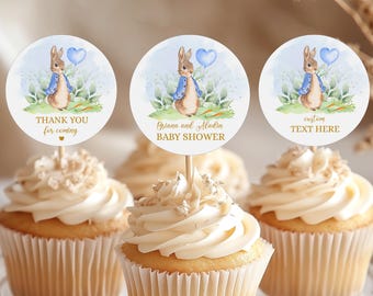 May include: Three white cupcakes with vanilla frosting and gold sprinkles topped with round paper cupcake toppers featuring a watercolor illustration of Peter Rabbit holding a blue balloon. The toppers have text that reads "Thank you for coming", "Griana and Madin Baby Shower", and "Custom Text Here".
