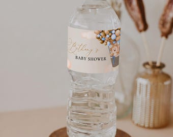 Peut inclure: Une bouteille d'eau en plastique transparent avec une étiquette personnalisée représentant un ours en peluche brun dans une montgolfière faite de ballons bleus et beiges. L'étiquette porte le texte Bethany's BABY SHOWER.