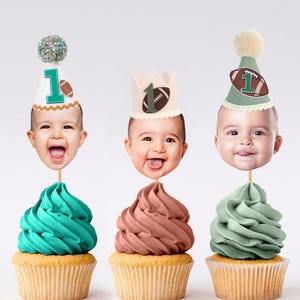Puede incluir: Tres cupcakes rematados con recortes de caras de bebé con gorros de fiesta. El gorro izquierdo es blanco con un número 1 verde y un balón de fútbol americano. El centro es una corona con un 1 verde y un balón. El derecho es verde salvia.