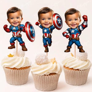 Può includere: Tre topper per cupcake con il viso di un bambino sovrapposto a un'immagine di cartone animato di Capitan America. I topper sono in cima a cupcake con glassa bianca.