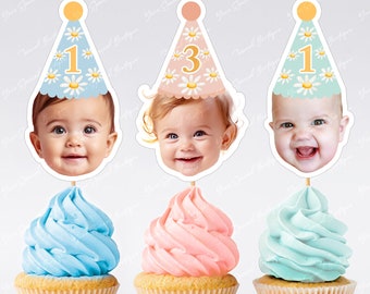 May include: Three cupcake toppers featuring a baby's face with a birthday hat. The hats are blue, pink, and green with white daisies and the numbers 1 and 3.