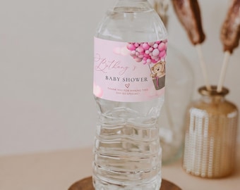 Pode incluir: Uma garrafa de água de plástico transparente com um rótulo rosa apresentando um ursinho de pelúcia num balão de ar quente feito de balões cor-de-rosa. O texto diz: Bethany's BABY SHOWER, um coração e THANK YOU FOR MAKING THIS DAY SO SPECIAL.