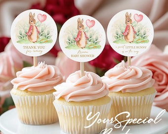 May include: Three pink frosted cupcakes with white cupcake liners. Each cupcake has a round, white paper circle with a watercolor illustration of a bunny rabbit holding a pink balloon. The text on the circles reads "Thank you for coming", "Briana Baby Shower", and "A sweet little bunny is on the way".