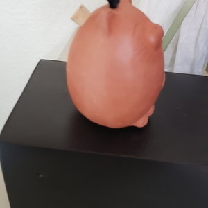 May include: A terracotta piggy bank ornament with a black ribbon and a wooden stopper. The piggy bank is sitting on a black box.