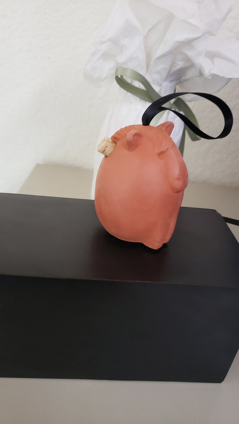 May include: A terracotta-colored ceramic animal figurine with a cork stopper. The figurine is shaped like a pig and has a brown cork stopper in the back.