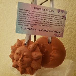 May include: Two terracotta ornaments, one shaped like a sun and the other like a crescent moon, with a tag that reads "Directions for Use" and includes instructions for using essential oils. The tag also includes the website Etsy.com/shop/TheAromaStoreCompany.
