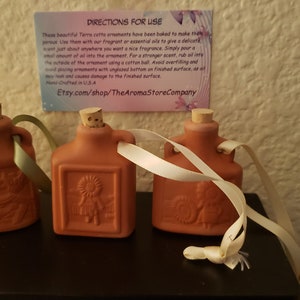 May include: Three terracotta ornaments shaped like small bottles with cork stoppers and white ribbon ties. Each bottle has a different design embossed on the front. The ornaments are on a dark surface with a card that reads "DIRECTIONS FOR USE" and "Etsy.com/shop/TheAromaStoreCompany".