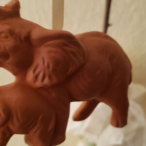 May include: A terracotta sculpture of two elephants, one larger than the other, standing side-by-side. The elephants are a reddish-brown color and have detailed features.