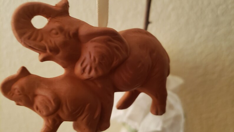 May include: A terracotta sculpture of two elephants, one larger than the other, standing side-by-side. The elephants are a reddish-brown color and have detailed features.