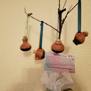 May include: Four small terracotta brown and black ceramic ornaments with cork stoppers hanging from a branch. The ornaments are labeled "The Aroma Store Company" and have directions for use.