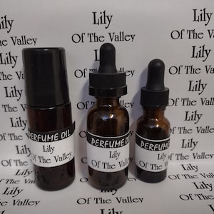 May include: Three perfume oil bottles of varying sizes. The bottles are amber-colored glass with black caps and labels that read "PERFUME OIL Lily Of The Valley". One bottle has a rollerball top, and the others have droppers.