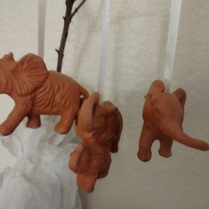 May include: Three terracotta elephant ornaments hanging from white strings. The elephants are all facing different directions and have a rustic, hand-crafted look.
