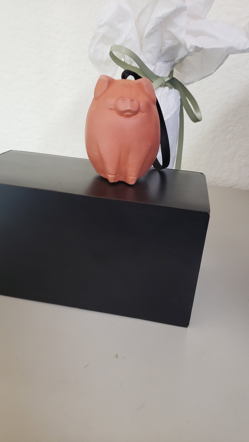 May include: A terracotta pig figurine with a black string attached to its head. The pig is sitting on a black box.
