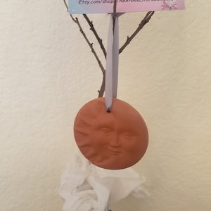 May include: A terracotta sun ornament with a smiling face, hanging from a branch with a gray ribbon. The ornament is a diffuser for essential oils. The text on the card reads "Directions for Use" and "Etsy.com/shop TheAromaStoreCompany".