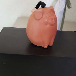 May include: A terracotta piggy bank with a black string attached to the top. The piggy bank is sitting on a black box.