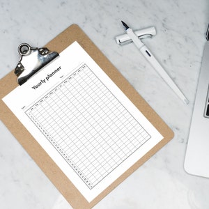 May include: A blank yearly planner on a clipboard with a white pen. The planner has columns for each month of the year and rows for each day of the month.