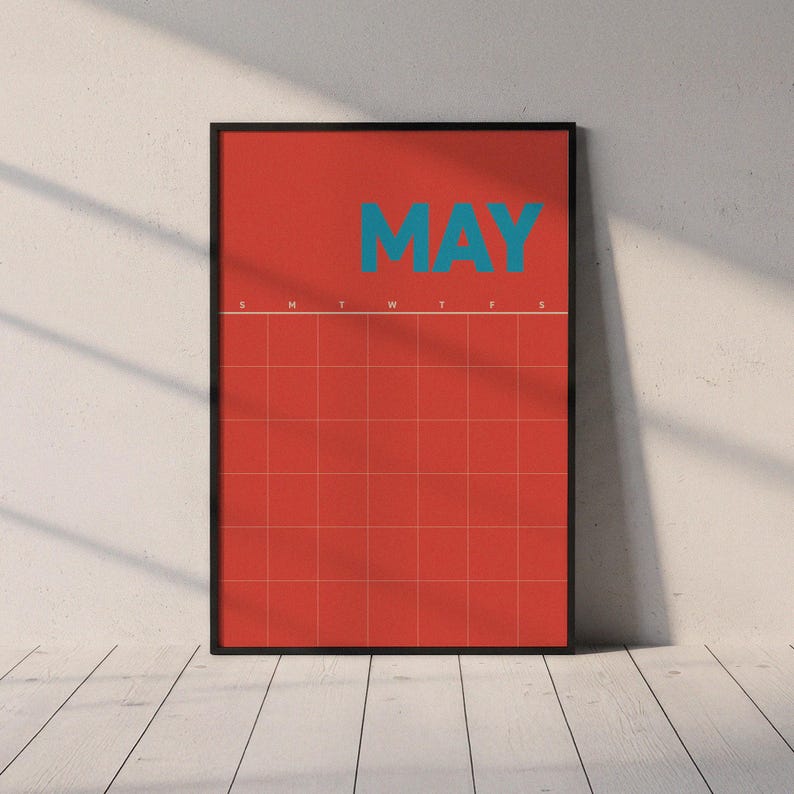 May include: A framed calendar print for May. The background is coral with a grid pattern. The word "MAY" is in teal block letters at the top. The calendar grid is framed in a black border. The print is displayed on a white wall.