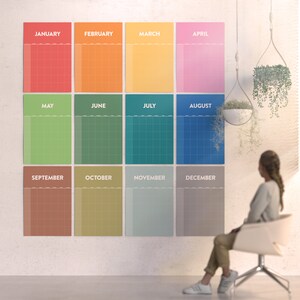 May include: A wall calendar with a grid layout and a different color for each month. The months are labeled January, February, March, April, May, June, July, August, September, October, November, and December. The calendar is hanging on a white wall.