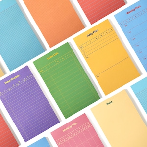 May include: A collection of colourful paper notepads featuring various layouts including grid, lined, and specific planning templates. The pads are labelled with text such as Daily Plan, Weekly Plan, To Do List, Time Tracker, Monthly Plan, and Plain.