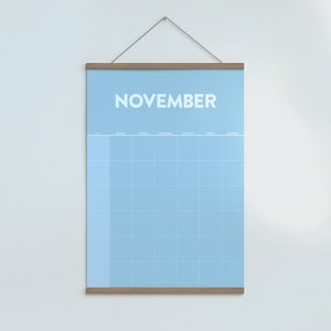 May include: A light blue monthly calendar with a wooden frame hanging on a white wall. The calendar is labeled "NOVEMBER" at the top and has a grid of squares for each day of the month.
