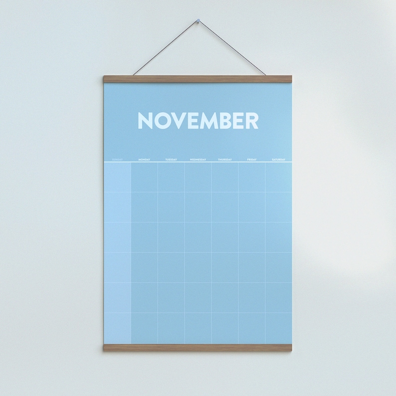 May include: A light blue monthly calendar with a wooden frame hanging on a white wall. The calendar is labeled "NOVEMBER" at the top and has a grid of squares for each day of the month.