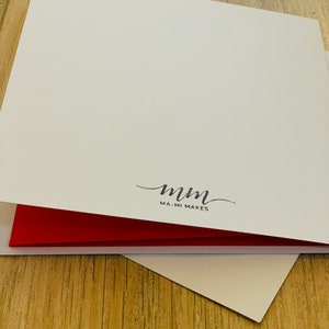 Puede incluir: Una pila de tarjetas de felicitaci&oacute;n blancas con interior rojo. Las tarjetas est&aacute;n abiertas, revelando el interior rojo. La esquina inferior derecha de la tarjeta es visible. Las palabras "mm MA-MI MAKES" est&aacute;n impresas en escritura negra.