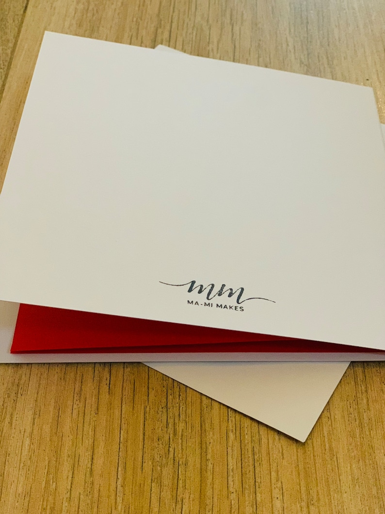 Puede incluir: Una pila de tarjetas de felicitaci&oacute;n blancas con interior rojo. Las tarjetas est&aacute;n abiertas, revelando el interior rojo. La esquina inferior derecha de la tarjeta es visible. Las palabras "mm MA-MI MAKES" est&aacute;n impresas en escritura negra.