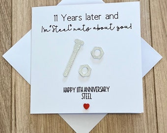 May include: A white card with the text "11 Years later and I'm "Steel" nuts about you!" with a silver bolt and two silver nuts. The card also says "Happy 11th Anniversary Steel" with a red heart.