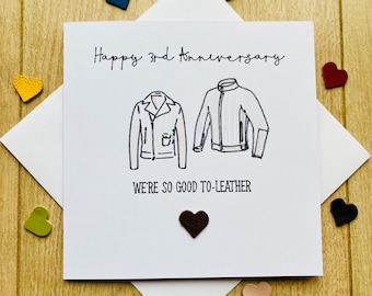 May include: A white card with the text "Happy 3rd Anniversary" and "We're so good to-leather" with two drawings of leather jackets. A brown heart is attached to the card.