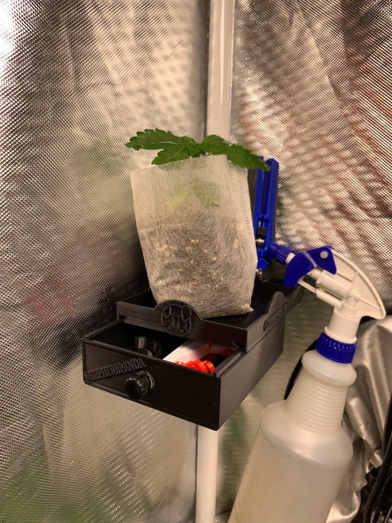 May include: A black 3D printed grow tent accessory with a drawer that says "Super Panda" on it. A small plant in a white grow bag is attached to the accessory with a blue clamp. A white spray bottle with a blue nozzle is also attached to the accessory.