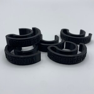 May include: Six black plastic rings with the text "@SUPERBRAND" printed on them.