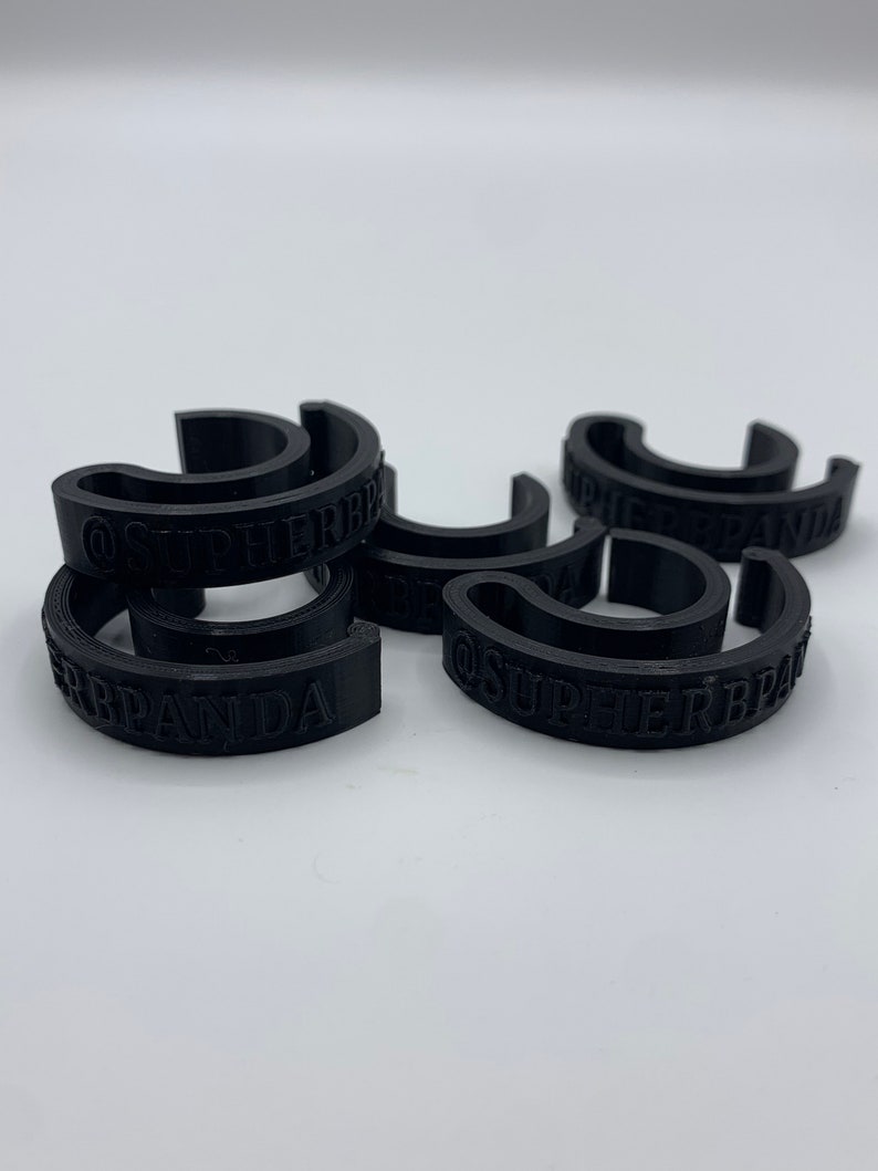 May include: Six black plastic rings with the text "@SUPERBRAND" printed on them.