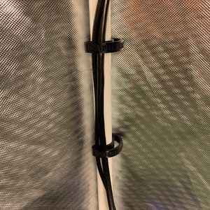 May include: Two black cables are secured to a white pole with two black cable ties. The cable ties have the text "SUPERIOR" printed on them.