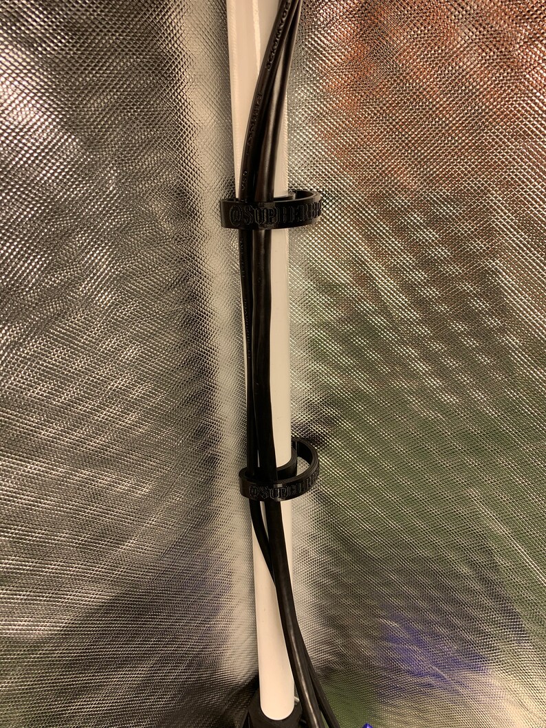 May include: Two black cables are secured to a white pole with two black cable ties. The cable ties have the text "SUPERIOR" printed on them.
