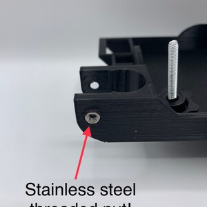May include: Close-up of a black 3D printed object with a stainless steel threaded nut. The nut is visible in the lower left corner of the image.